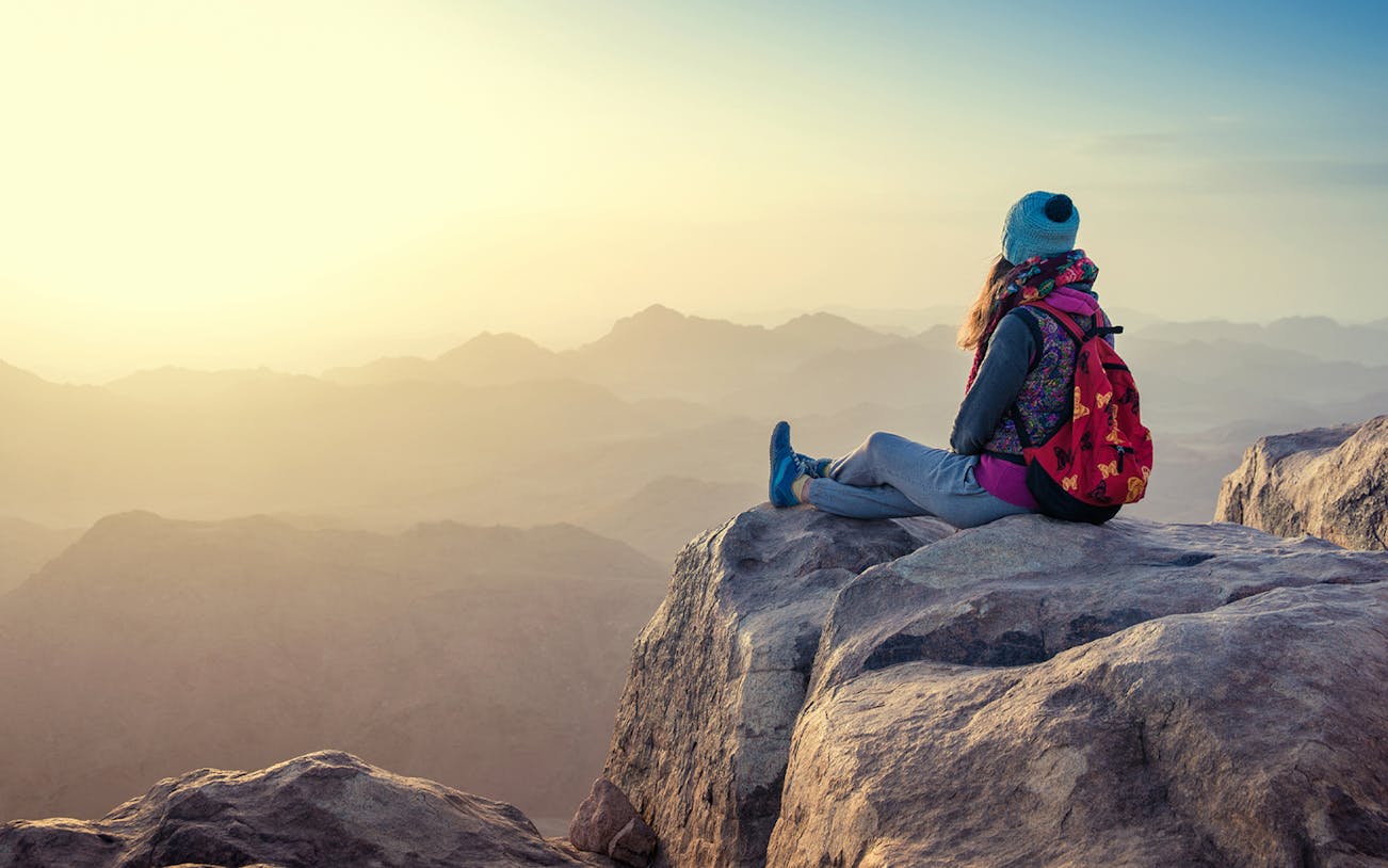 Traveler sitting on a mountain peak at sunrise, Sharm-El-Sheikh hike.
