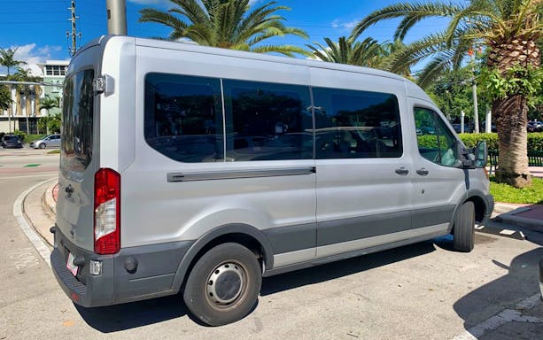 Tour transfer van for Everglades Airboat Tour parked under palm trees.