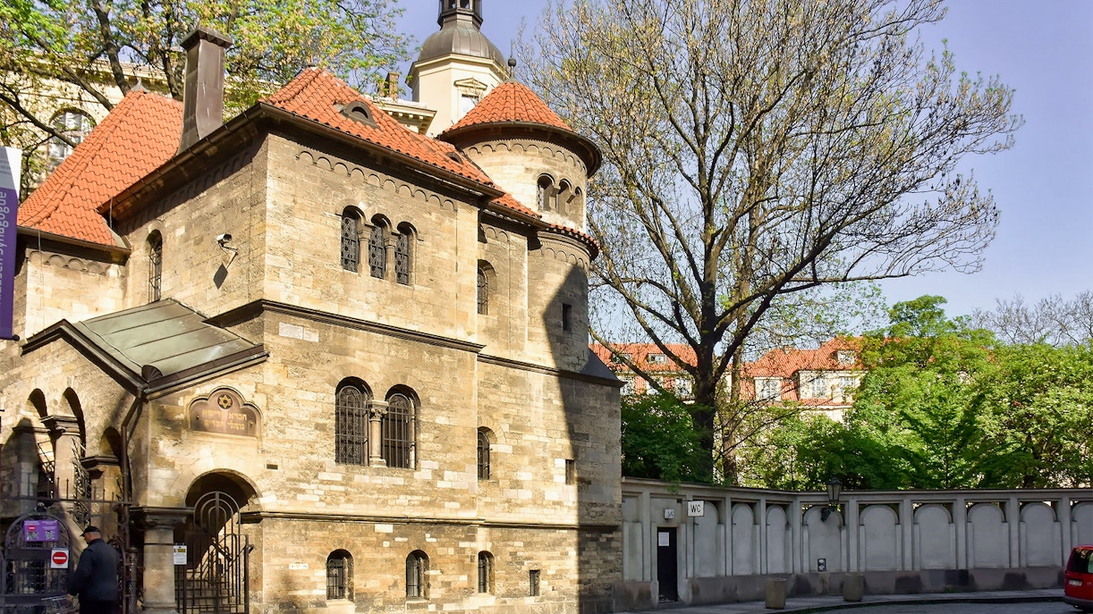 Jewish Quarter building with red-tiled roof in Prague, surrounded by trees.