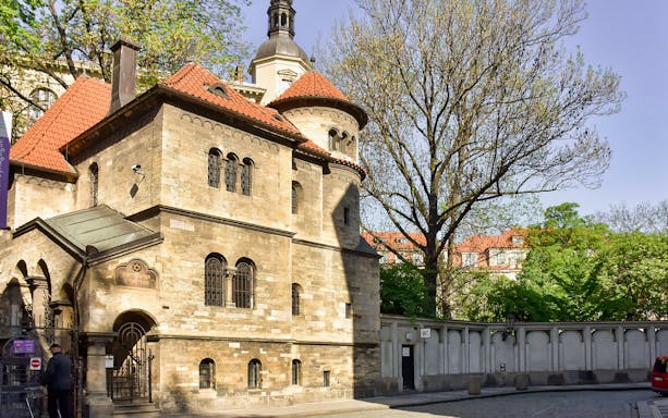 Jewish Quarter building with red-tiled roof in Prague, surrounded by trees.