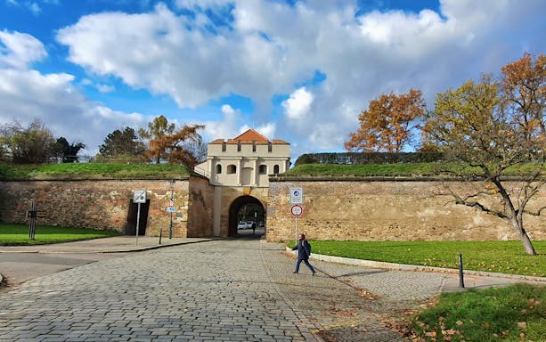 Vyšehrad Fort entrance with cobblestone path in Prague, autumn trees in background.