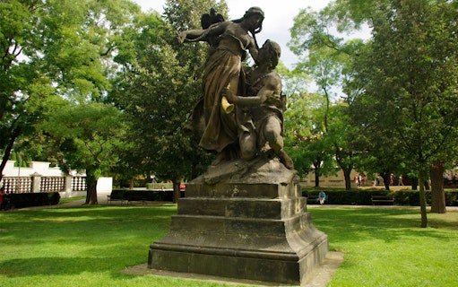 Statue in Vyšehrad Fort park, Prague, surrounded by trees and greenery.