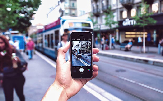 Person holding a smartphone capturing a tram on a street in Amsterdam.