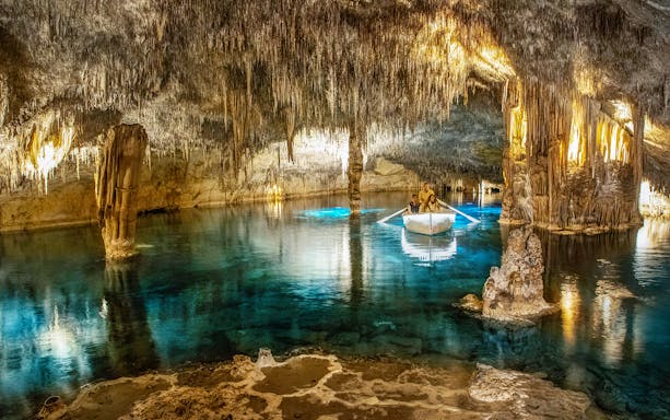 Boat tour inside the illuminated Caves of Drach, Mallorca, showcasing stalactites and clear water.