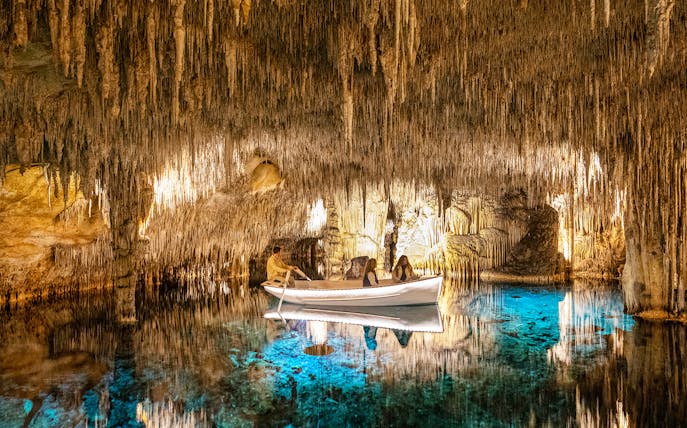 Boat tour inside the illuminated Caves of Drach, showcasing stalactites and clear blue water.