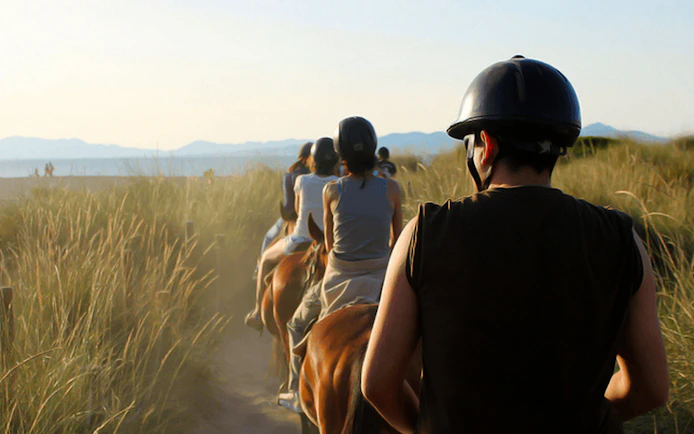 Group horse riding along a beach path in Mallorca.