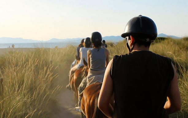 Group horse riding along a beach path in Mallorca.