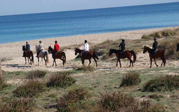 Horseback riders on a sandy beach trail by the sea in Mallorca.