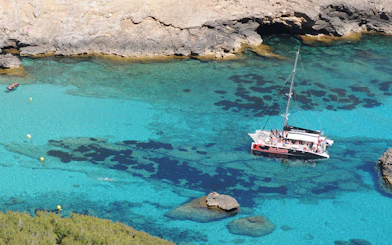Catamaran sailing in clear waters of Pollensa Bay, Mallorca, with rocky coastline.
