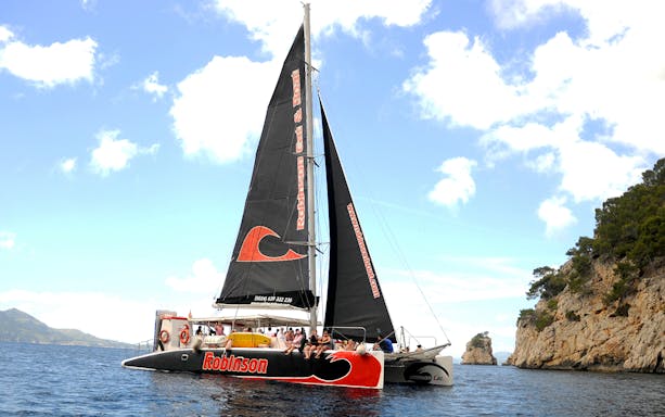 Robinson catamaran sailing in Pollensa Bay with passengers enjoying the view.