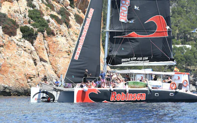 Robinson catamaran sailing near rocky cliffs in Pollensa Bay.