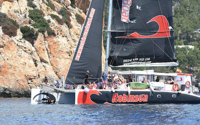 Robinson catamaran sailing near rocky cliffs in Pollensa Bay.