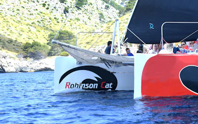 Robinson Catamaran sailing in Pollensa Bay with passengers enjoying the view.