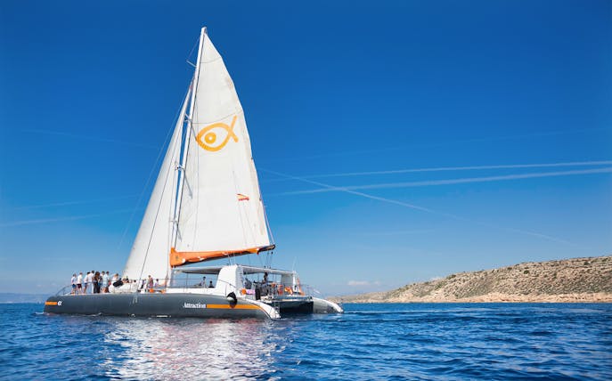 Catamaran sailing near Palma de Mallorca coastline with passengers on deck.