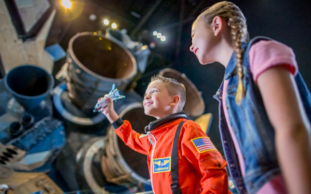 Child in astronaut suit holding model shuttle at Kennedy Space Center exhibit.