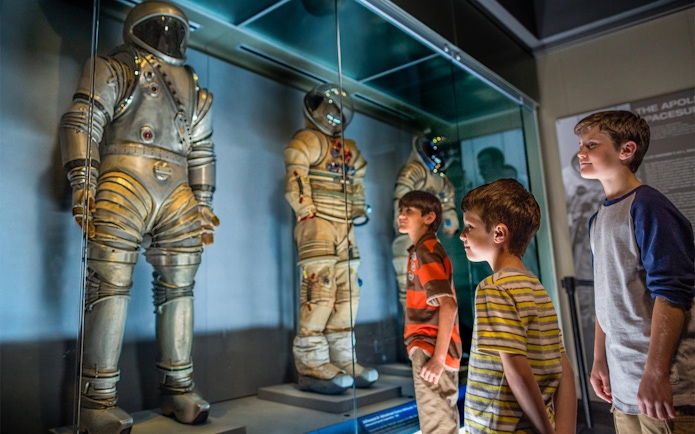 Children observing astronaut suits at Kennedy Space Center exhibit.