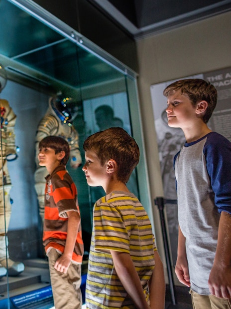 Children observing astronaut suits at Kennedy Space Center exhibit.