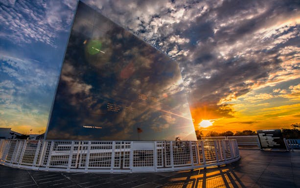 Kennedy Space Center memorial wall at sunset reflecting clouds and sky.
