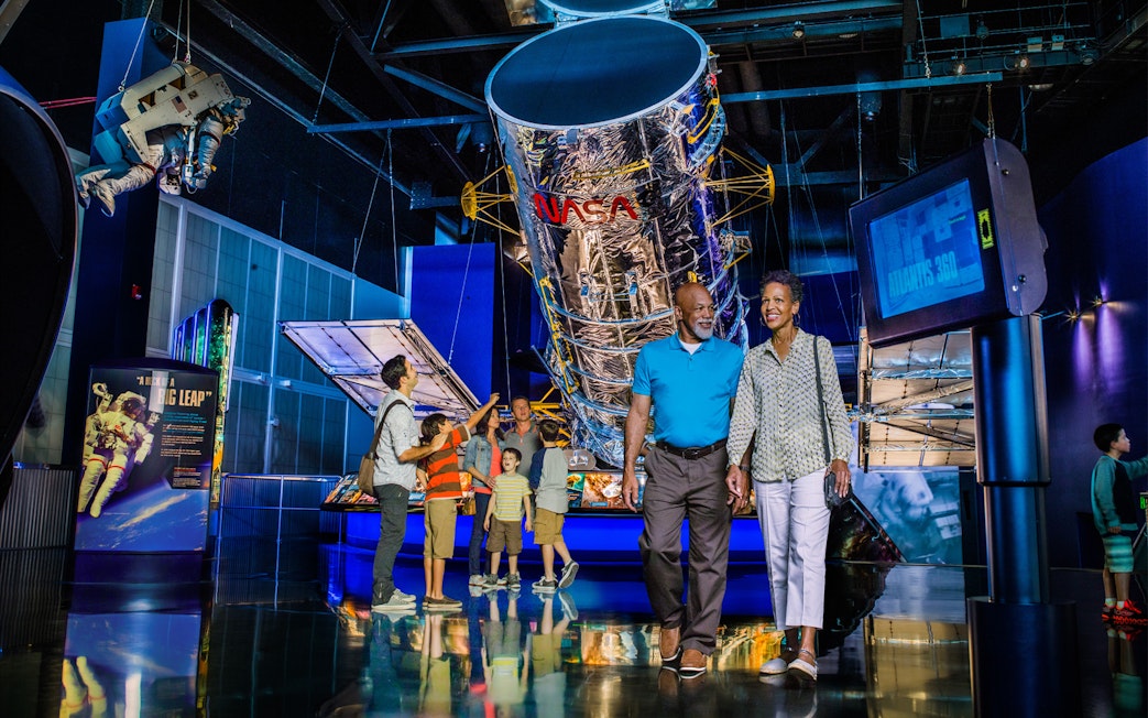 Visitors exploring exhibits at Kennedy Space Center, including a large NASA telescope display.