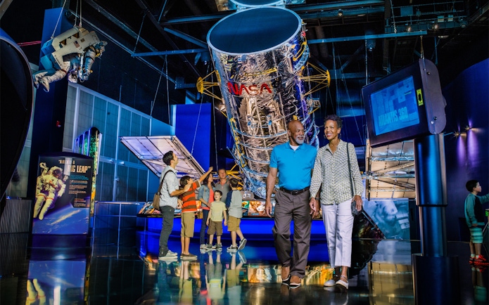 Visitors exploring exhibits at Kennedy Space Center, including a large NASA telescope display.