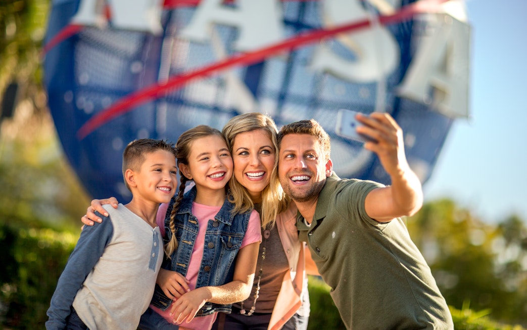 Family taking a selfie at Kennedy Space Center with NASA globe in background.