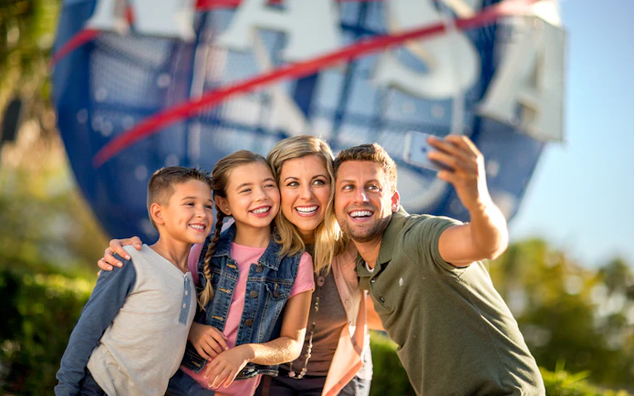 Family taking a selfie at Kennedy Space Center with NASA globe in background.
