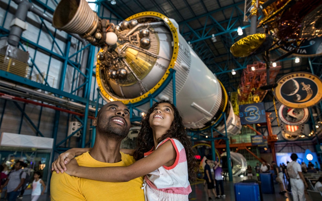 Father and daughter admiring a Saturn V rocket at Kennedy Space Center.