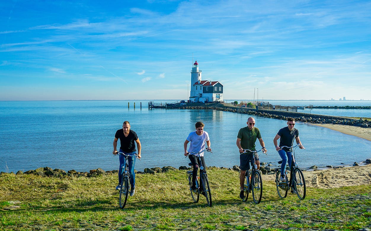 Cyclists riding along Volendam's coastline with a lighthouse in the background.