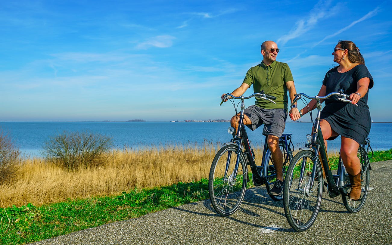 Couple cycling along a scenic path by the water in Volendam, Netherlands.