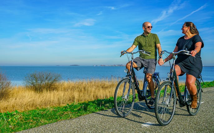 Couple cycling along a scenic path by the water in Volendam, Netherlands.