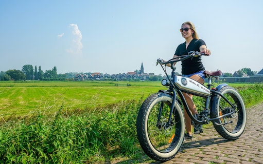 E-Fatbike rider on a path in Volendam countryside, Amsterdam in the background.