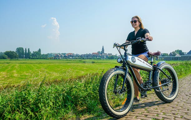 E-Fatbike rider on a path in Volendam countryside, Amsterdam in the background.