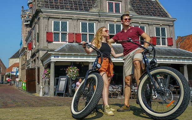 Couple with e-fatbikes in front of historic building in Volendam, Amsterdam countryside.