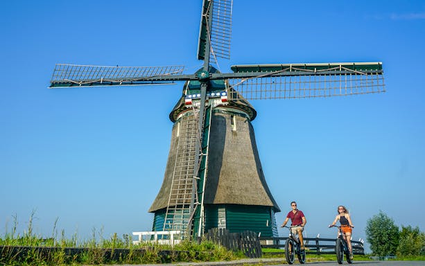 Cyclists on e-fatbikes near a traditional windmill in Volendam countryside, Amsterdam.