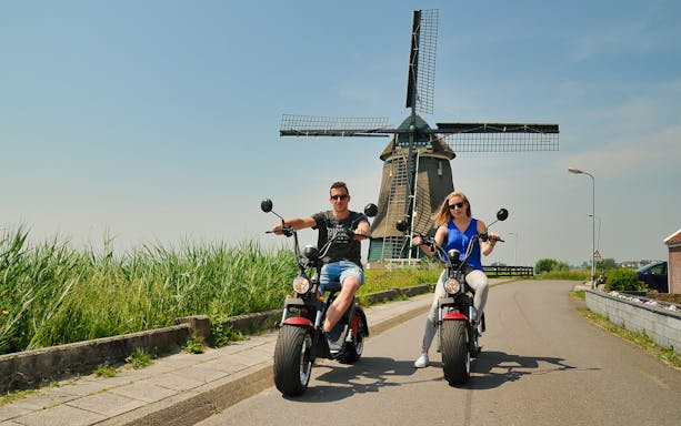 E-scooter riders near a windmill in Volendam countryside, Amsterdam.