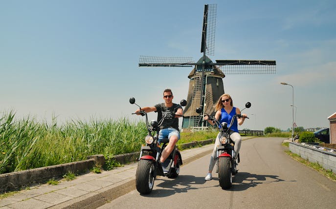 E-scooter riders near a windmill in Volendam countryside, Amsterdam.