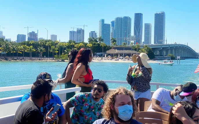 Tourists enjoying a Miami skyline cruise with cityscape and bridge in the background.