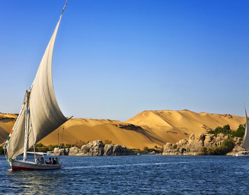 Felucca sailing on the Nile River with desert landscape near Cairo.