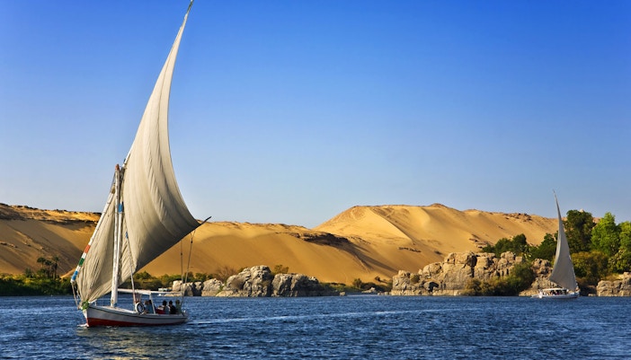 Felucca sailing on the Nile River with desert landscape near Cairo.