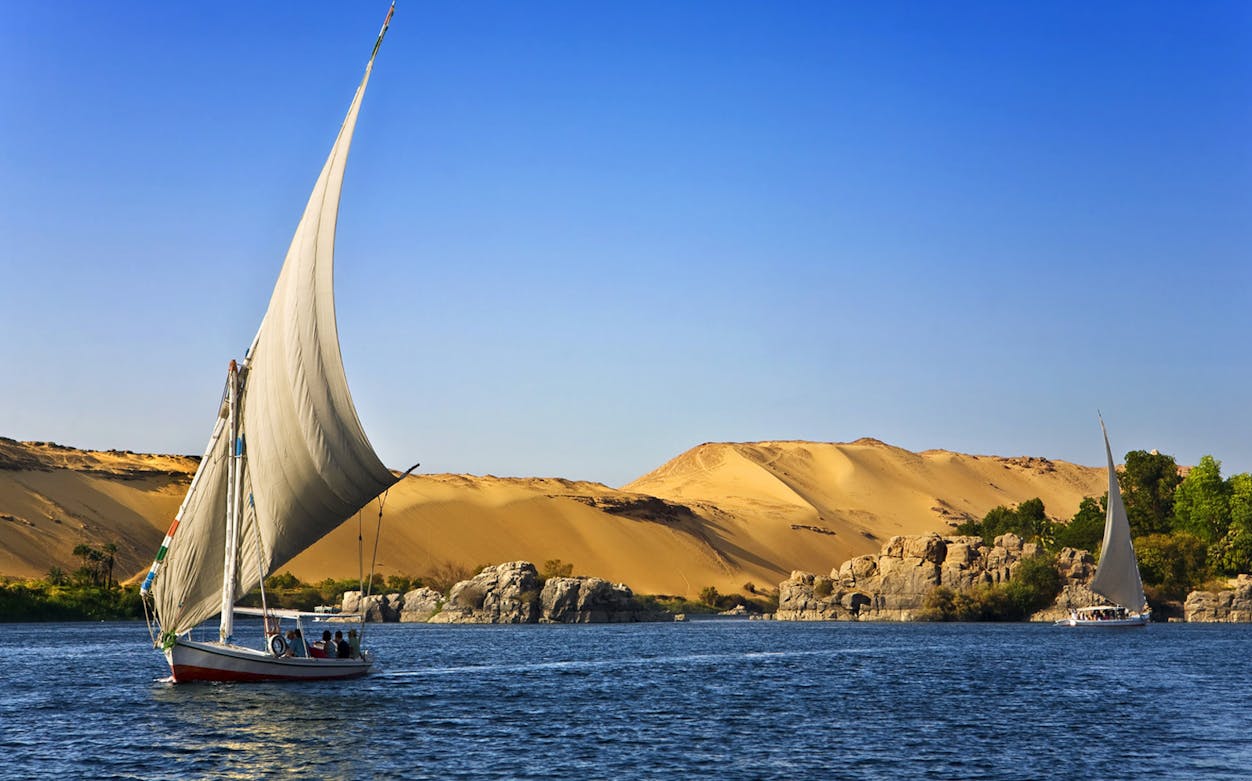 Felucca sailing on the Nile River with desert landscape near Cairo.