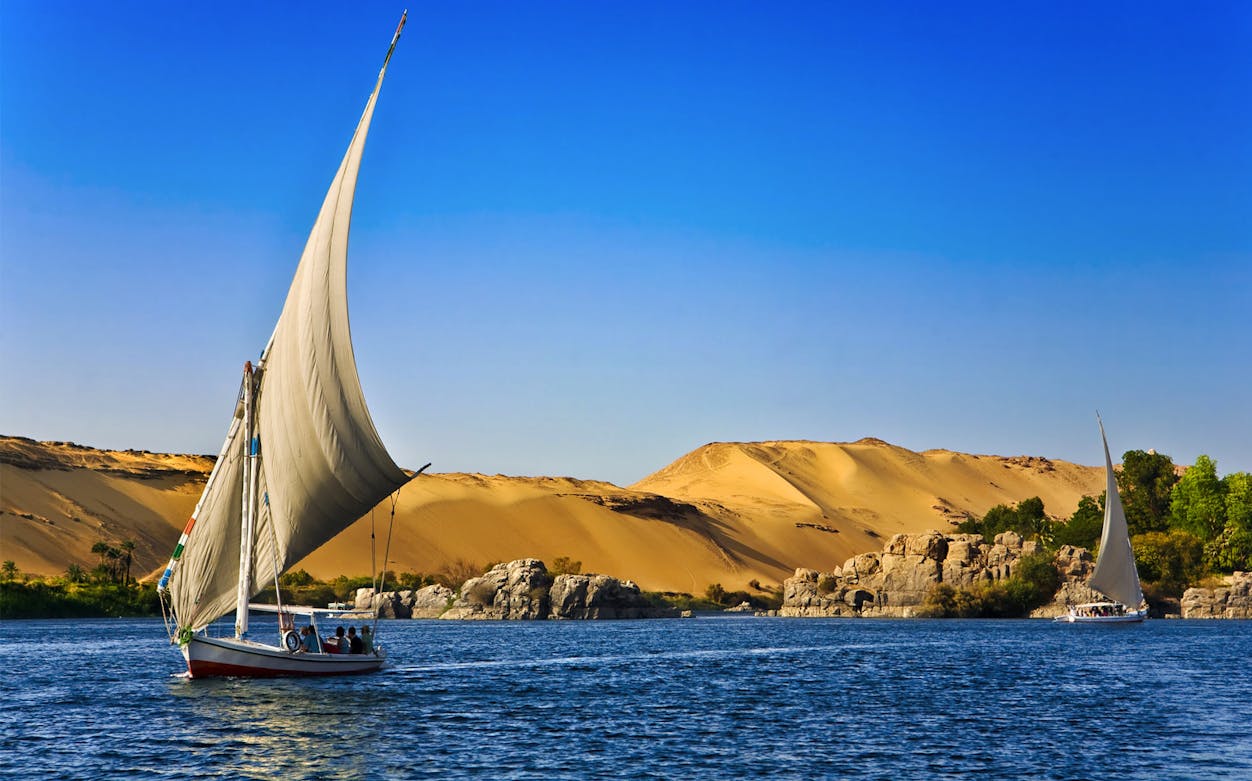 Felucca sailing on the Nile River with desert landscape in the background, Egypt.