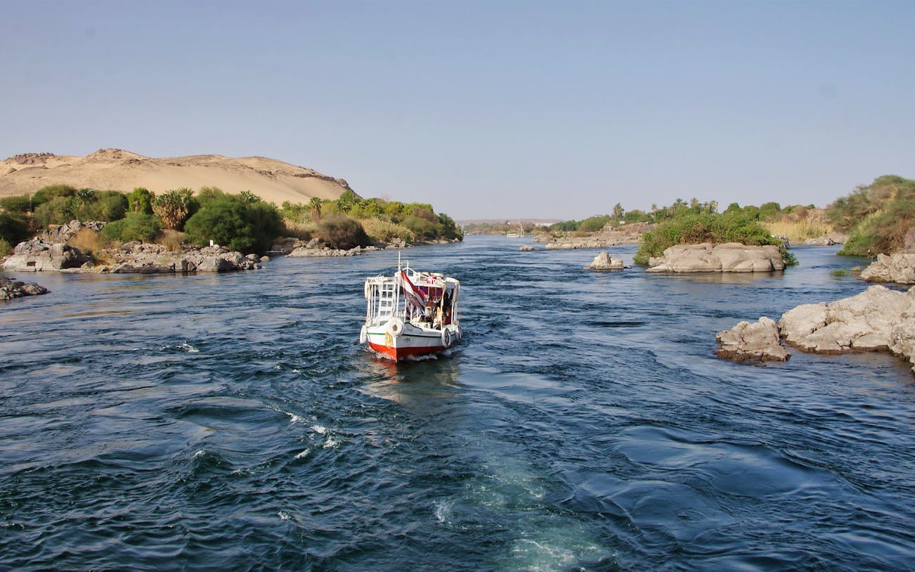 Sailing boat on the Nile River near Cairo with desert landscape in the background.