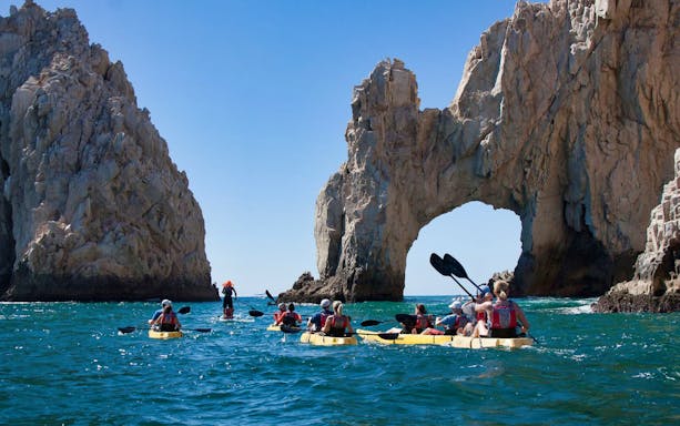 Kayakers in glass bottom boats near the Arch of Cabo San Lucas.