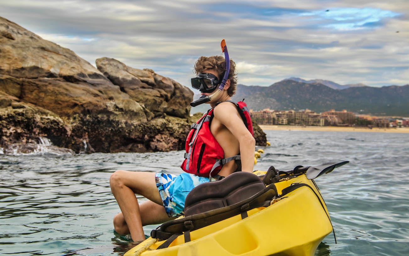 Kayaker in snorkel gear near rocky shore on Glass Bottom Kayaks & Snorkeling Tour at the Arch.