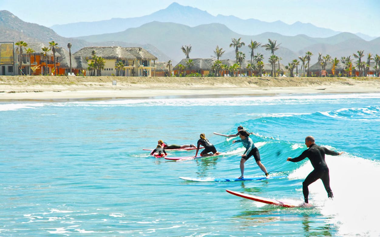 Surfers taking lessons at Cerritos Beach with mountains in the background.