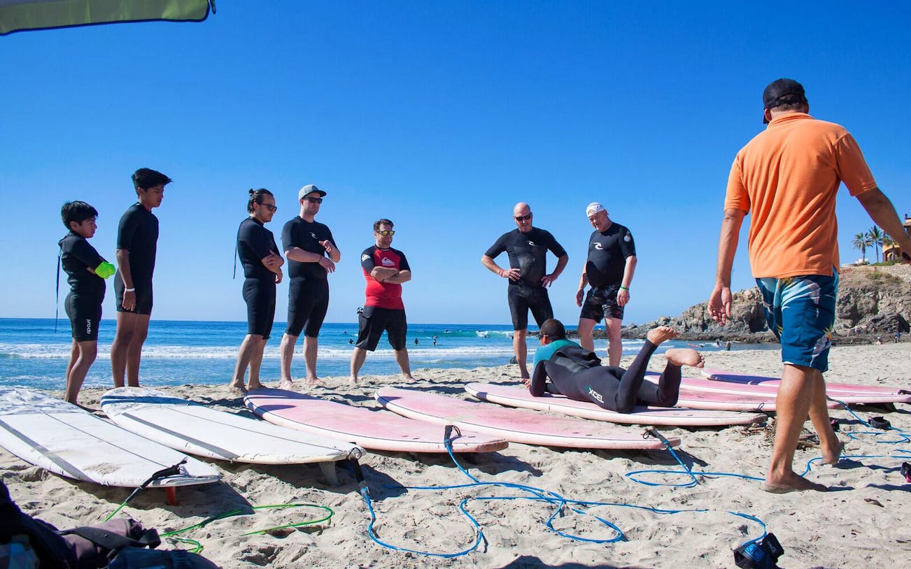 Group receiving surf lesson on Cerritos Beach, Baja California Sur, with surfboards on sand.