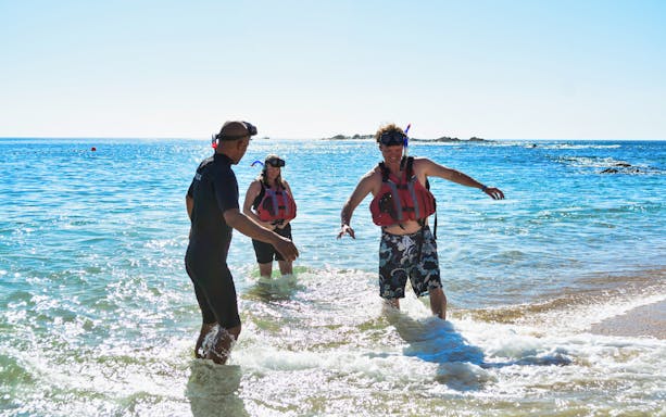 Snorkelers in life vests entering the ocean for a guided snorkel tour.
