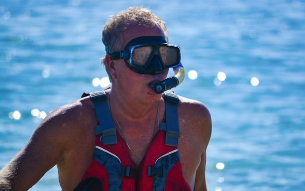 Snorkeler in red vest and mask during guided snorkel tour in clear blue water.