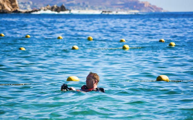Snorkeler in ocean near yellow buoys during guided tour.