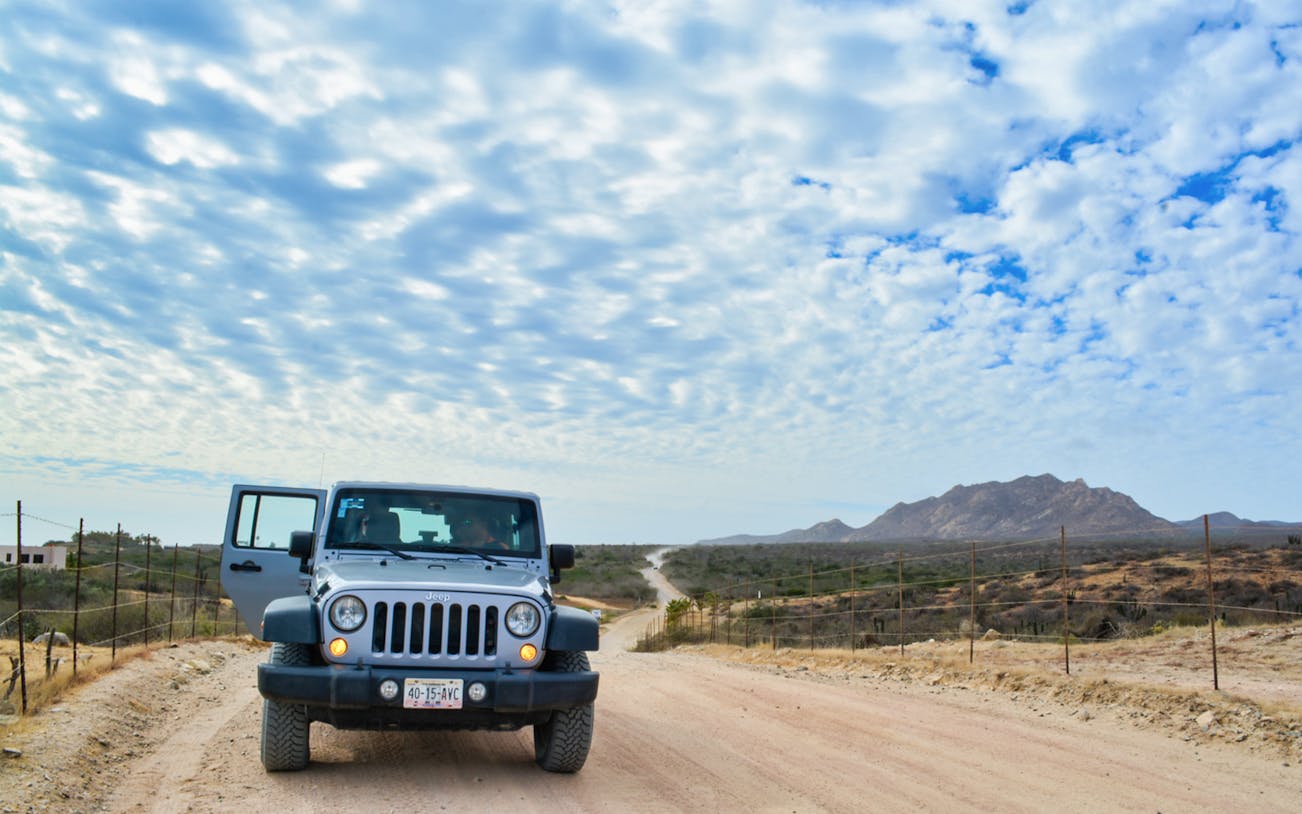 Jeep on a dirt road with mountains in the background during Baja offroad tour.